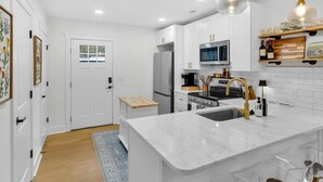 A modern kitchen with white cabinetry, a marble island, stainless steel appliances, and a wooden bench.