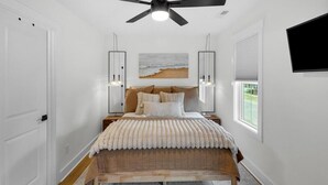 A bedroom with a bed, a ceiling fan, a window, and a wall-mounted TV.