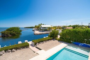 A beachfront property with a swimming pool, a dock with boats, and a small island with a house. - Oceanfront home with a pool, dock, grill, scenic balconies, games, W/D, & AC (Tavernier)