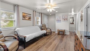 Ein Schlafzimmer mit einem Bett, zwei Stühlen, einem kleinen Tisch, einem Deckenventilator und Bildern an den Wänden.