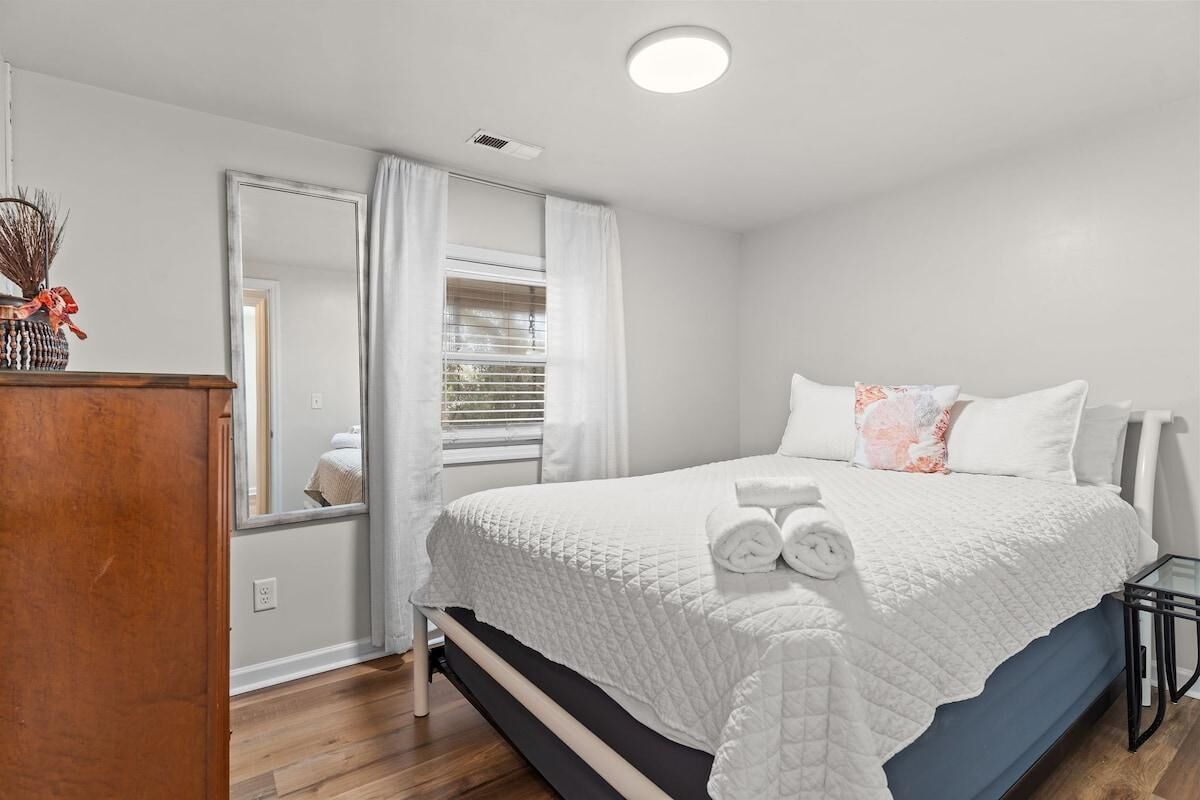 Un dormitorio con cama, cómoda, espejo y ventana con cortinas.