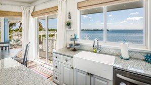 Una cocina con un amplio ventanal con vista al mar, un lavamanos y una zona de comedor con vistas.