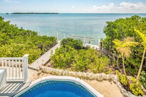 A swimming pool with a view of the ocean, surrounded by greenery and a wooden deck. - Amazing waterfront home with private beach, dock, pool, WiFi & outdoor kitchen (Cudjoe Key)