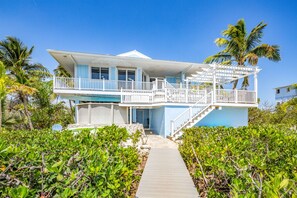 A two-story beachfront house with a balcony, a covered porch, and a wooden walkway leading to the entrance. - Amazing waterfront home with private beach, dock, pool, WiFi & outdoor kitchen (Cudjoe Key)