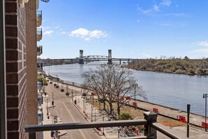 A river with a bridge, a sidewalk, and a building with balconies. - Pups and Pints - Water View - We Love Dogs (Wilmington)