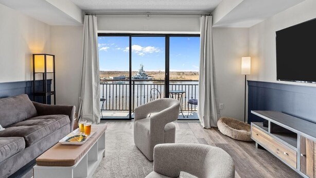 Une chambre d’hôtel moderne dotée d’un balcon, d’un canapé, d’une télévision et d’une table à manger avec des verres.