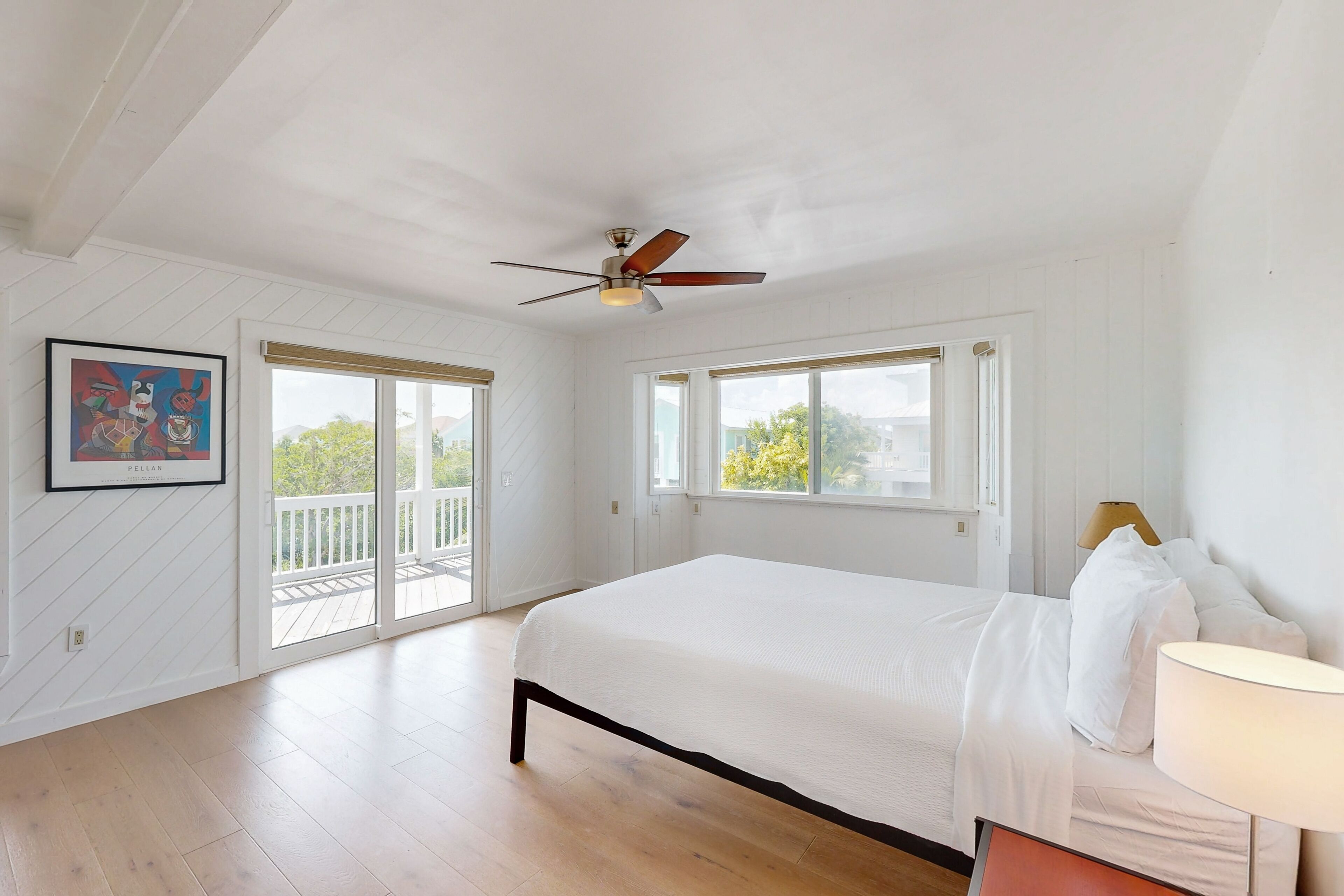 A bedroom with a large bed, a ceiling fan, and a balcony door.