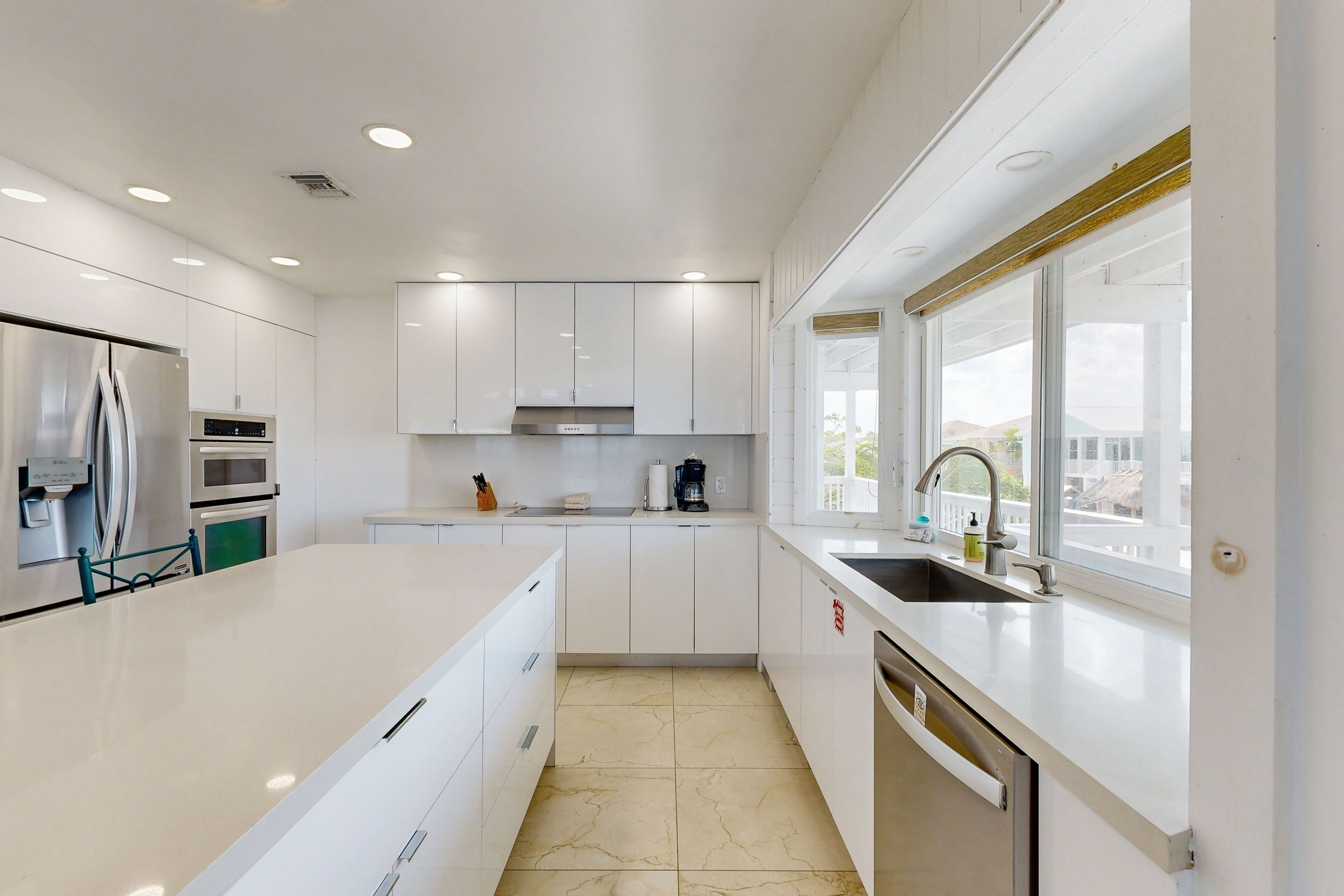 A modern kitchen with white cabinetry, a stainless steel refrigerator, an oven, a dishwasher, and a window providing a view of the outdoors.