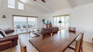 Een ruime woonkamer met een grote houten tafel, een leren bank en een plafondventilator.