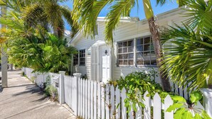 A white house with a picket fence, surrounded by lush greenery and palm trees. - Old Town Key West classic with private saltwater pool & enclosed patio- by shops (Key West)