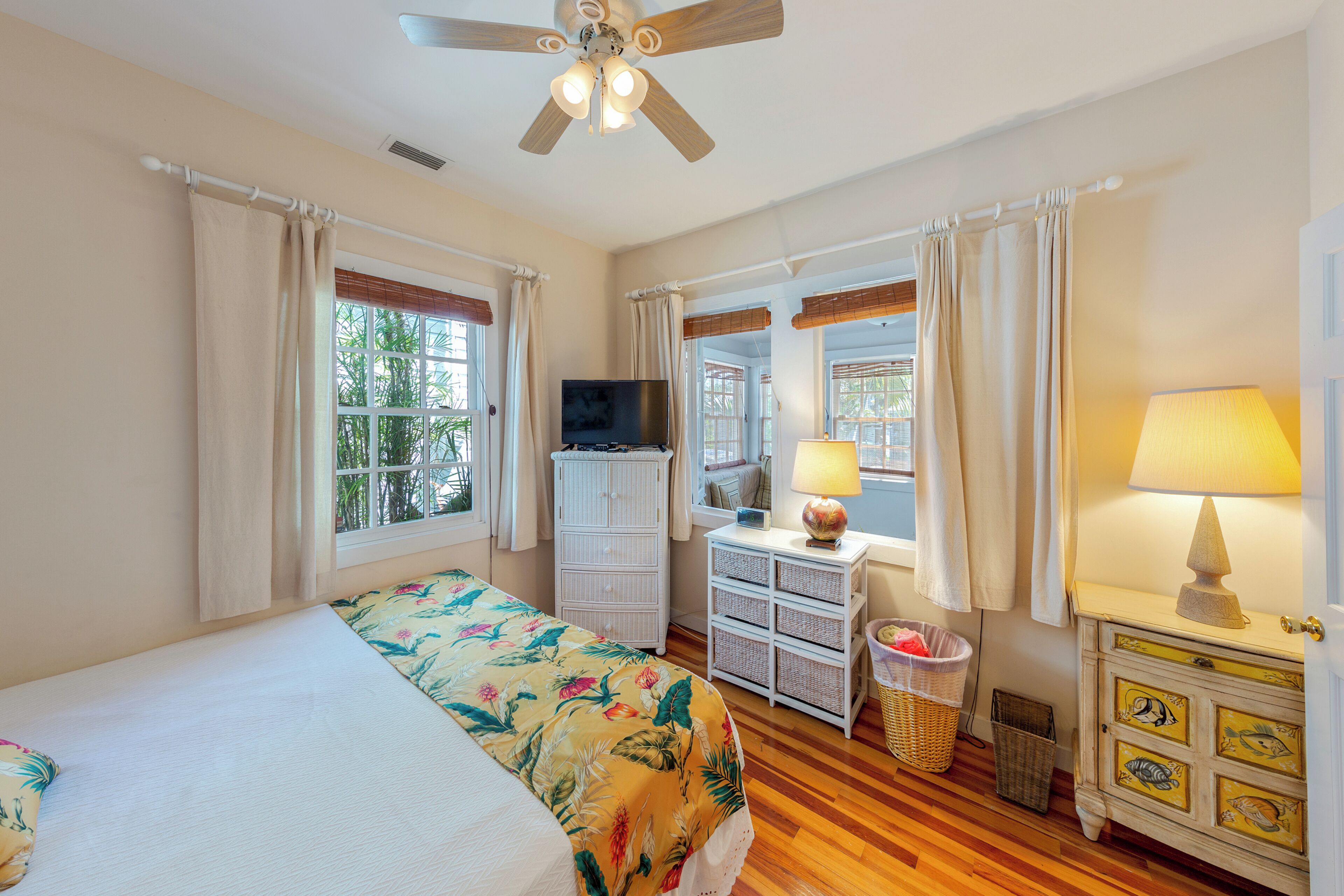 A bedroom with a bed, a television, a dresser, and a window with curtains.