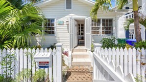 A white house with a white picket fence, a welcome mat, and a security sign. - Old Town Key West classic with private saltwater pool & enclosed patio- by shops (Key West)