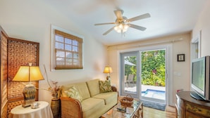 A living room with a ceiling fan, a sofa, a glass coffee table, a TV, and a view of a pool through a sliding glass door. - Old Town Key West classic with private saltwater pool & enclosed patio- by shops (Key West)