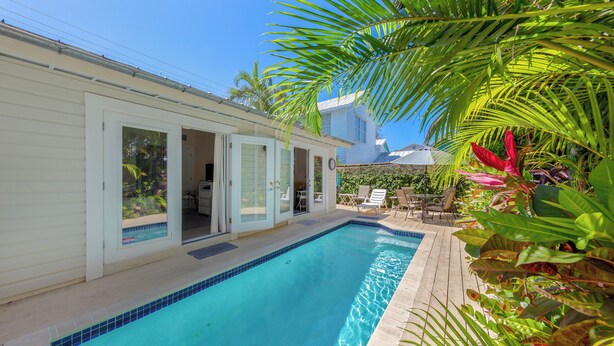 A swimming pool adjacent to a house with sliding glass doors, surrounded by tropical plants and a clear blue sky. - Old Town Key West classic with private saltwater pool & enclosed patio- by shops (Key West)