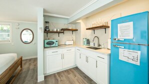 Una cocina compacta con armarios blancos, un refrigerador azul y un microondas.