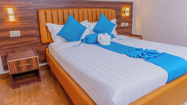 A neatly made bed with white and blue bedding, a wooden headboard, and bedside tables with lamps. - Arise Sunshine Hotel (Narok)