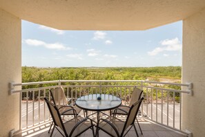 Un balcon avec une table ronde et des chaises, une vue sur la verdure et un ciel dégagé.