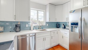 Een moderne keuken met witte kasten, roestvrijstalen apparatuur, een vaatwasser en een koffiezetapparaat.