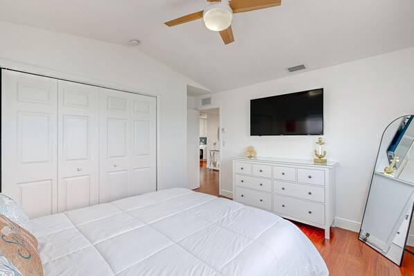 Ein Schlafzimmer mit einem großen Bett, einem Deckenventilator, einem Fernseher, einem Schminktisch und einem Kleiderschrank.