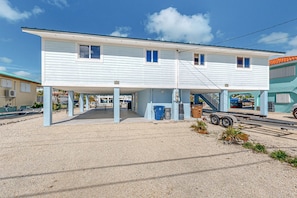 A two-story building with a covered parking area and a gravel driveway. - Waterfront coastal duplex w/ balcony views, gas grill, washer & dryer, WiFi (Marathon)