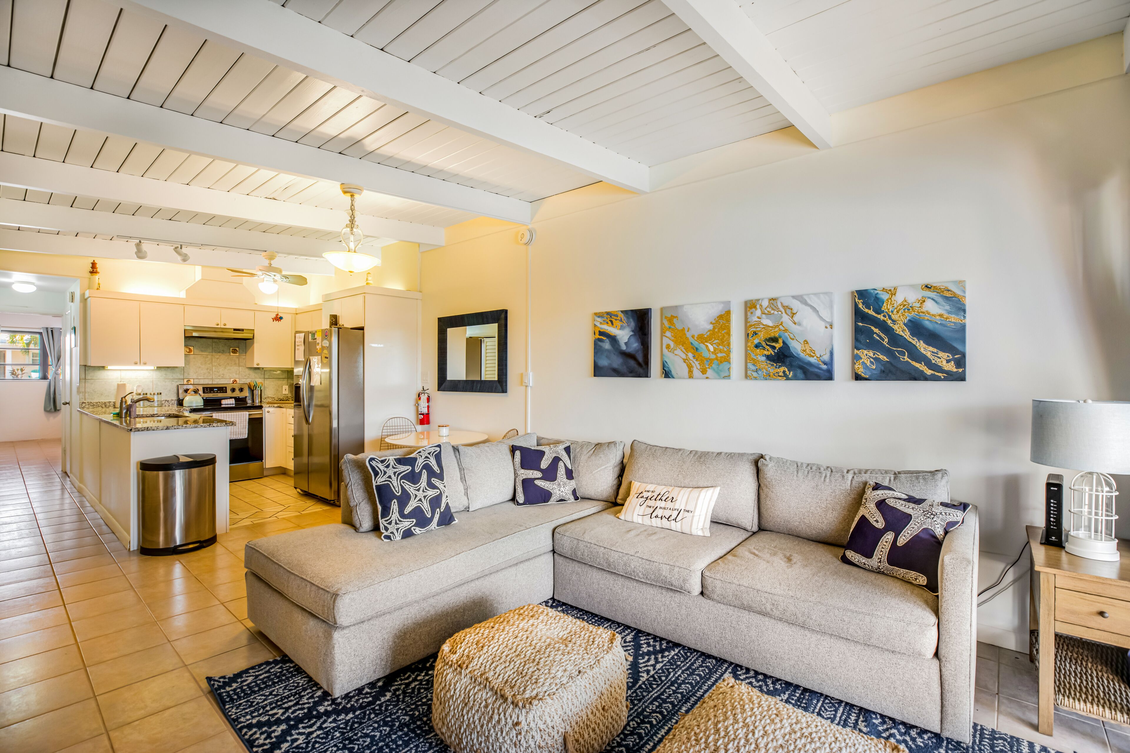 A modern living room with a sofa, ottoman, and a kitchen in the background.