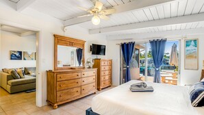 A bedroom with a large bed, wooden dresser, and a ceiling fan. There is a TV on the wall and a view of the outdoors through the window. - Waterfront home with gorgeous patio, WiFi, gas grill, & great location (Key Colony Beach)