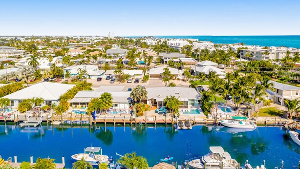 A marina with boats docked, surrounded by residential buildings and palm trees. - Waterfront home with gorgeous patio, WiFi, gas grill, & great location (Key Colony Beach)