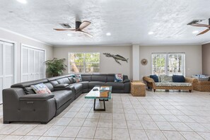 Ein geräumiges Wohnzimmer mit Ecksofa, einem kleinen Sofa, einem Glastisch und einem Deckenventilator.