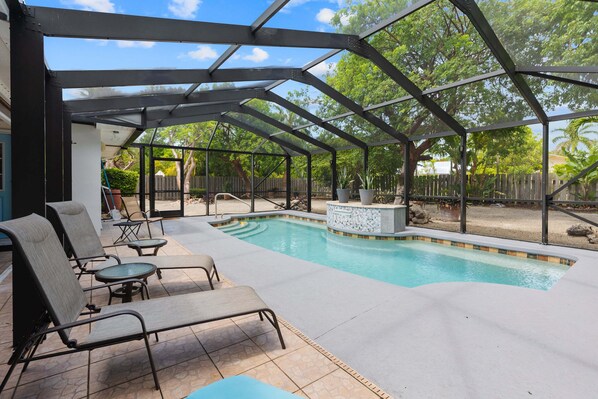Ein überdachter Pool im Freien mit Liegestühlen und einer Terrasse mit Steinplatten.