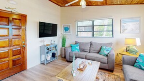 A living room with a wooden ceiling, a grey sofa, a coffee table, and a television. - Renovated waterfront duplex with canal access, deck, water views & central AC (Marathon)