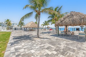 A paved walkway with thatched umbrellas, palm trees, and a view of the ocean. - Condo in Marathon with waterfront pool, patio, kayak & sundeck (Marathon)