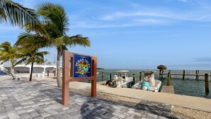 A beachside area with a sign for Ocean Islands Fishing Village, a boat dock, and a palm tree. - Condo in Marathon with waterfront pool, patio, kayak & sundeck (Marathon)