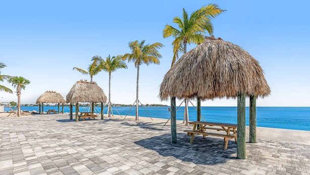A beachside patio with thatched umbrellas and wooden benches, overlooking the sea. - Snowbird-friendly sound view condo with open layout, patio, W/D, & AC (Marathon)