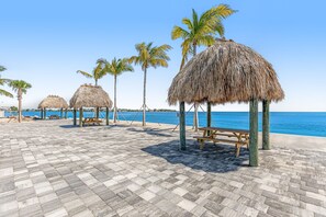 A beachside patio with thatched umbrellas and wooden benches, overlooking the sea. - Snowbird-friendly sound view condo with open layout, patio, W/D, & AC (Marathon)