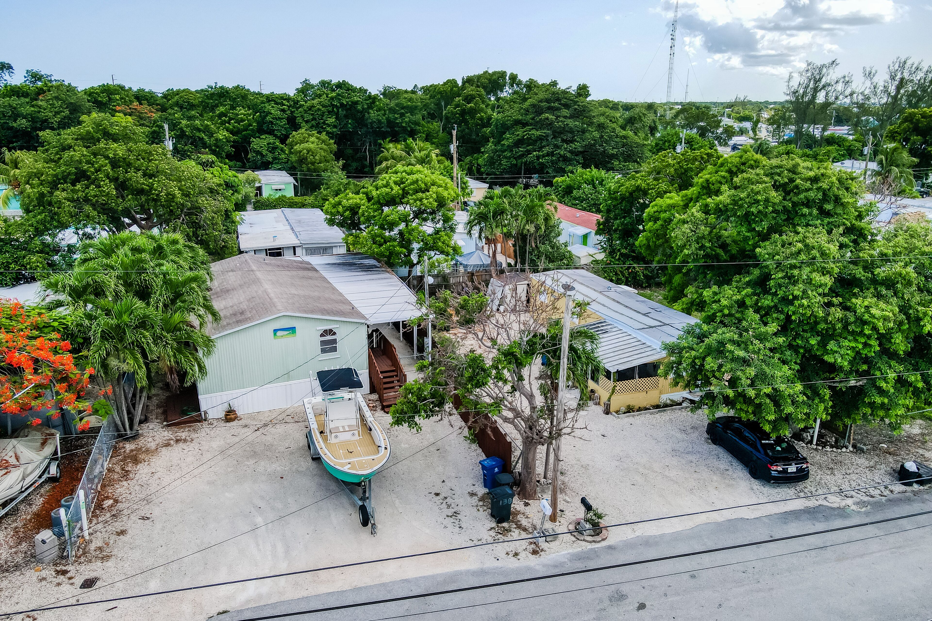 A residential area with houses, a boat, and a car parked on a sandy driveway.