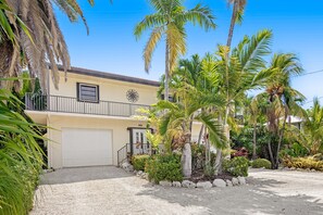 A two-story building with a garage, surrounded by palm trees and various plants. - Waterfront home with ocean views, dock, & private outdoor pool (Marathon)