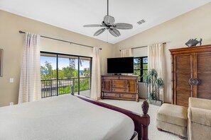 A bedroom with a large bed, a ceiling fan, a TV, a wooden dresser, and a view of the outdoors. - Waterfront home with ocean views, dock, & private outdoor pool (Marathon)