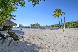 A beach with lounge chairs, a thatched umbrella, and a view of the water.