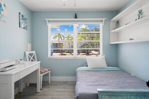 A bedroom with a bed, a desk, a chair, a window with blinds, and a shelf with decorative items. - Waterfront Home w/ Private Dock, Outdoor Shower & Home Office - Dog-Friendly (Marathon)