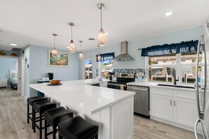 A modern kitchen with a large island, bar stools, stainless steel appliances, and pendant lighting. - Waterfront Home w/ Private Dock, Outdoor Shower & Home Office - Dog-Friendly (Marathon)