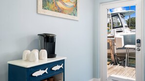 Et værelse med kaffemaskine, et skab med fiskegreb og en dør, der fører til et udendørs område med en båd.