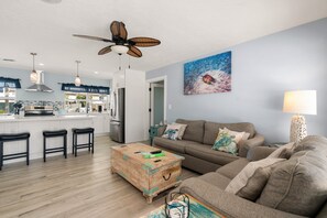 Eine moderne Küche mit einer zentralen Kochinsel, Barhocker, einem Holztisch, einer Couch und einem Deckenventilator.