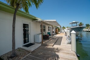 Eine Holzterrasse mit Gartenmöbeln, ein Boot, das im Wasser liegt, und ein Gebäude mit weißer Fassade.