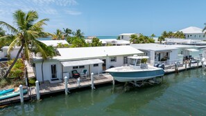 A waterfront property with a dock, a boat, and a small building with a porch. - Waterfront Home w/ Private Dock, Outdoor Shower & Home Office - Dog-Friendly (Marathon)