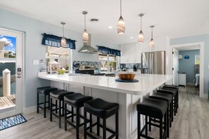 A modern kitchen with a large island, bar stools, pendant lighting, and a view of the outside. - Waterfront Home w/ Private Dock, Outdoor Shower & Home Office - Dog-Friendly (Marathon)