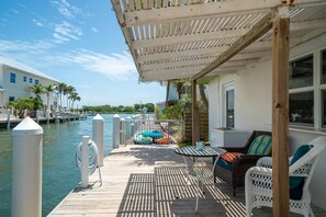 A wooden dock leading to a pool area with lounge chairs and a covered seating area.