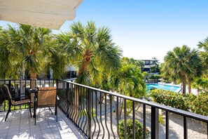 A balcony with a view of a swimming pool, surrounded by palm trees and a building in the background. - Second Floor Condo with Shared Pool, Shared Dock, Central AC, and WiFi (Marathon)