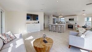 A modern living room with a wooden coffee table, a grey sofa, and a kitchen area with white cabinets and a central island. - Modern waterfront home with balcony, patio, grill, W/D, & easy Atlantic access (Marathon)