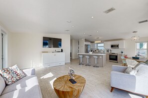 A modern living room with a wooden coffee table, a grey sofa, and a kitchen area with white cabinets and a central island. - Modern waterfront home with balcony, patio, grill, W/D, & easy Atlantic access (Marathon)