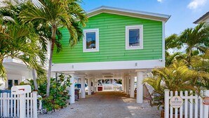 A green house with a covered porch, white fence, and palm trees. - Modern waterfront home with balcony, patio, grill, W/D, & easy Atlantic access (Marathon)